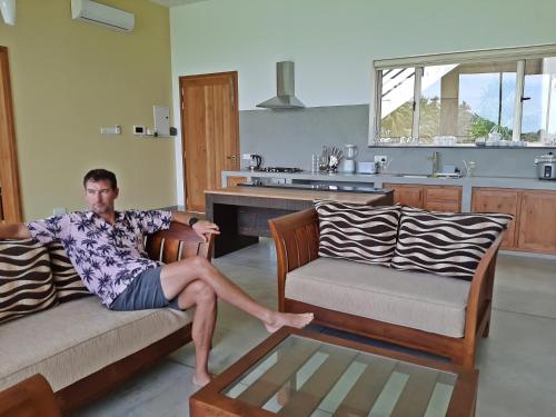 a man sitting on a couch in a living room at Sugoi House in Unawatuna