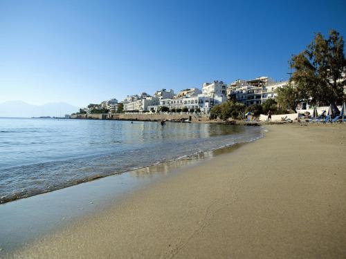 a beach with buildings in the background and the ocean at Victoria Hotel in Agios Nikolaos