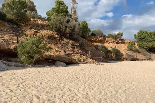 a sandy beach next to a rocky hill with trees at Accogliente casetta a Calaverde, Pula. in Pula