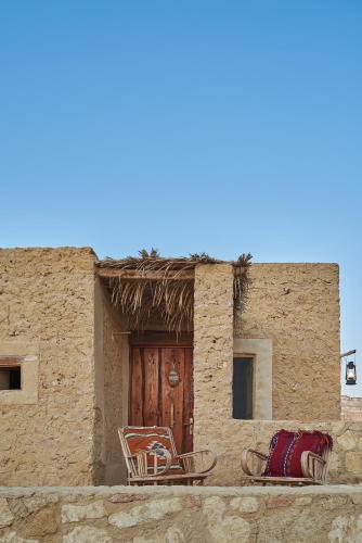 a building with two chairs and a wooden door at Talist Siwa in Siwa