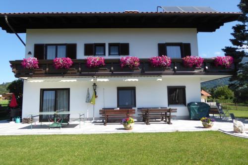 a white house with two benches and pink flowers at Pension Paßler in Seeboden