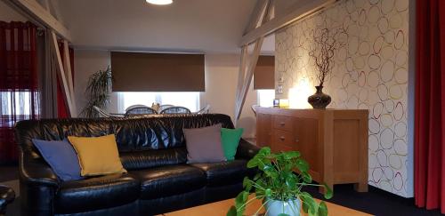 a living room with a black leather couch with colorful pillows at Apartment Campinor in Pelt