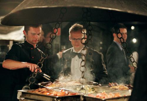 Dois homens numa cozinha a preparar comida num grelhador. em Agat Hotel em Łódź