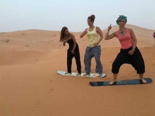 three women standing on surfboards in the desert at Sunset Camp Merzouga in Merzouga