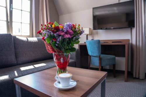 a vase of flowers on a table with a cup of coffee at Apart Neptun in Gdańsk