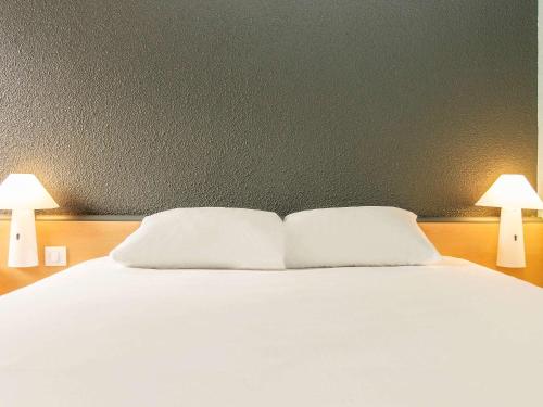 a bed with two white pillows on it with two lamps at ibis Falaise Coeur de Normandie in Falaise