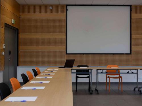 a conference room with a white screen and a table with chairs at ibis Styles Vierzon in Vierzon