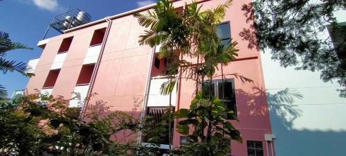 a pink building with trees in front of it at TK Thongrak Apartment in Hat Yai