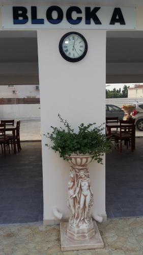 a plant in a vase in front of a building with a clock at Carisa Livadia Gardens in Livadhia