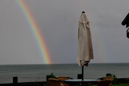 a table with an umbrella and a rainbow in the background at El Reflejo Lodge Spa - Queilen - Chiloé in Queilén