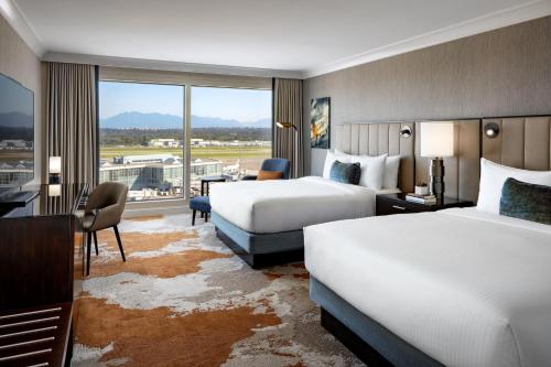 a hotel room with two beds and a desk at Fairmont Vancouver Airport In-Terminal Hotel in Richmond