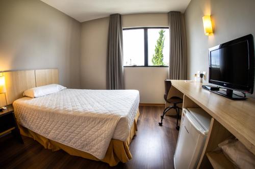 a hotel room with a bed and a flat screen tv at Hotel Campo Largo Express in Campo Largo