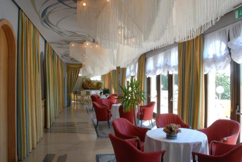 a dining room with tables and red chairs and chandeliers at Grand Hotel Astoria in Lavarone