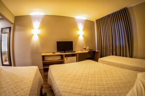 a hotel room with two beds and a desk with a television at Hotel Campo Largo Express in Campo Largo