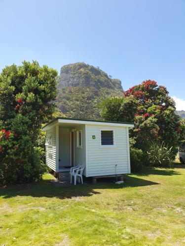 a small white shed with a mountain in the background at Punakaiki Beach Camp in Punakaiki