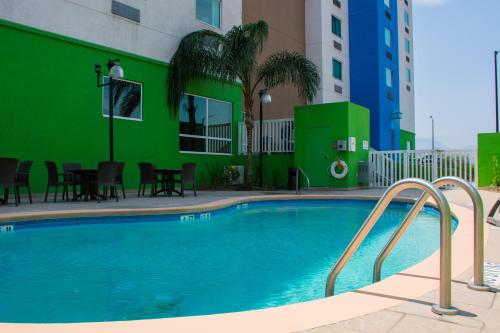 uma piscina em frente a um edifício com uma parede verde em Holiday Inn Express Saltillo Zona Aeropuerto, an IHG Hotel em Saltillo