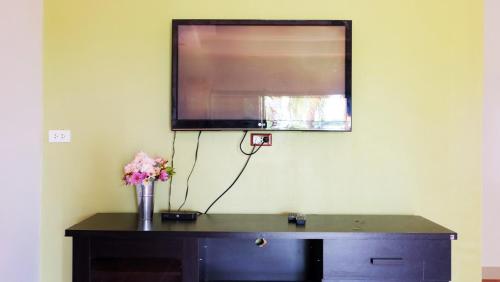 een televisie aan een muur met een vaas met bloemen op een bureau bij Narakorn House in Buriram