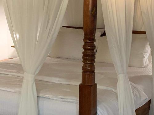 a bed with white curtains and a wooden post at Porsu in Canacona