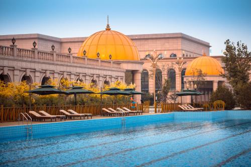 a building with a swimming pool with chairs and umbrellas at GUOCE Beijing Capital Airport Hotel & Convention Center in Shunyi