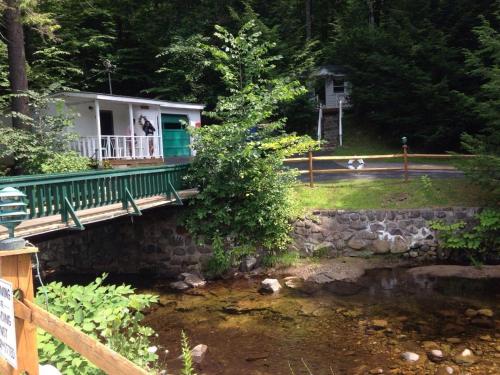 a house with a porch and a bridge over a creek at Brookside Motel & Cabins in Lake George