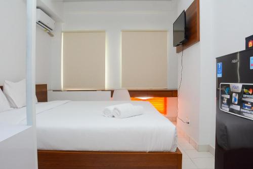 ein Schlafzimmer mit einem weißen Bett und einem Fernseher in der Unterkunft Comfy Studio Room at Patraland Urbano Apartment By Travelio in Bekasi