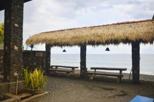 a beach with two benches and a thatch roof at Tasik Dumun Homestay and Waroeng in Amed