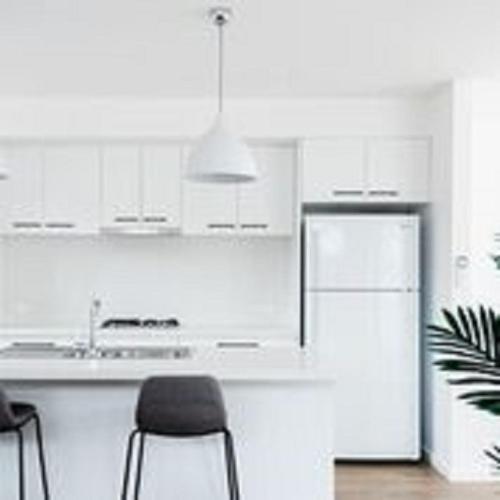 a kitchen with white cabinets and a refrigerator and chairs at Timor Street Apartments in Warrnambool