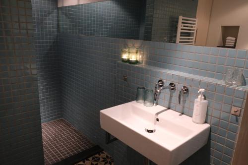 La salle de bains est pourvue de carrelage bleu, d'un lavabo et d'une douche. dans l'établissement B&B Radijs, à Beegden