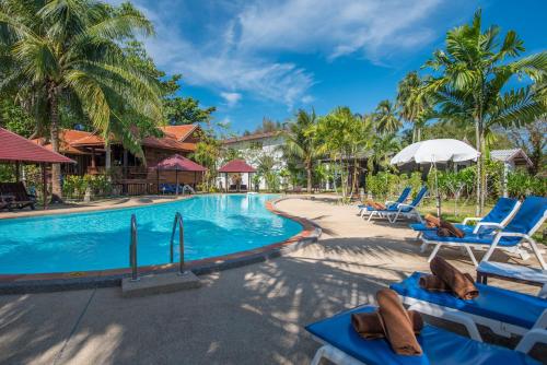 a pool at a resort with blue chairs and palm trees at ThaiLife Wellness & Meditation Resort- SHA Plus in Khao Lak