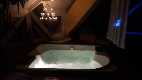 y baño con bañera y lámpara de araña. en Belíssima COBERTURA no Condomínio Switzerland, o conforto que toda família merece, en Campos do Jordão