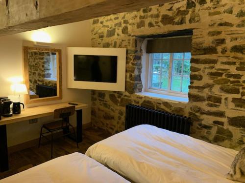 - une chambre dotée d'un mur en pierre avec un lit et un bureau dans l'établissement Trail Lodge, à Ballasalla