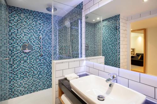 a bathroom with a sink and a shower with blue tiles at Holiday Inn London Heathrow - Bath Road, an IHG Hotel in Hillingdon