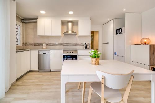 cocina blanca con mesa blanca y sillas en Hauzify I Apartament Rosa dels Vents, en Santa Susanna