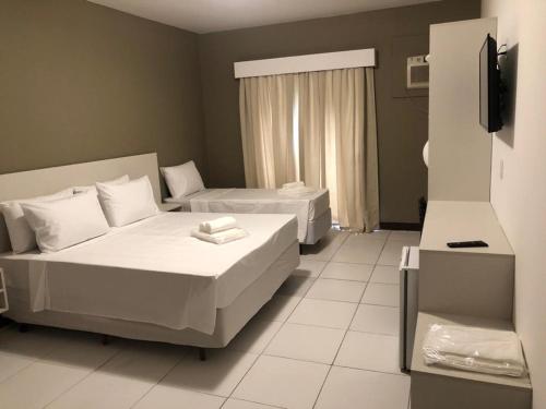 a hotel room with two beds and a television at Hotel Guarujá Inn Tropical in Guarujá