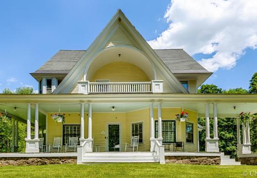 una casa amarilla con porche y sillas. en Noble House Inn, en Bridgton