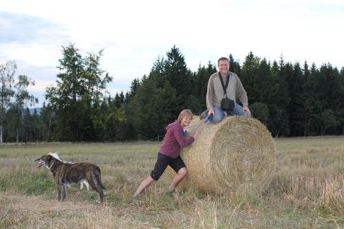 a man and a woman sitting on a hay bale with a dog at Słoneczna Zagroda - Sunny Ridge Farm in Łączna
