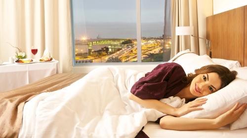 a woman laying in a bed with a window at Holiday Inn Guayaquil Airport by IHG in Guayaquil