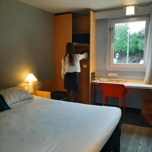 a woman is looking out of a window in a hotel room at ibis Rennes Cesson in Cesson-Sévigné