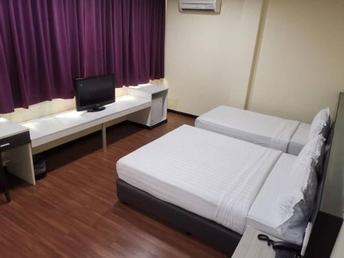 a room with two beds and a desk with a tv at Prince Hotel in Tawau