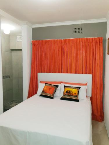 a bedroom with a white bed with an orange curtain at Lyronne Guest house, Shuttle and Tours in Cape Town