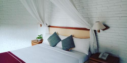 a bedroom with a white bed with pillows and a lamp at Puri Padi in Ubud