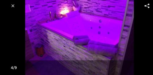 bañera púrpura en una habitación con pared de ladrillo en Le Menhir Jacuzzi Lit 200x200 en Le Cendre