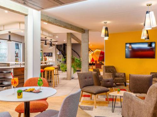 a lobby with chairs and tables and a yellow wall at Mercure Castres L'Occitan in Castres