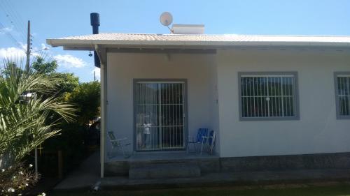 a white house with two chairs and a gate at Casa de praia na Gamboa - Garopaba SC in Garopaba