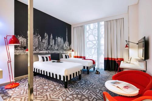 ibis Styles Dubai Airport Hotel في دبي: غرفة فندقية بسريرين وكرسي احمر