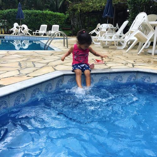 a little girl sitting on the edge of a swimming pool at Pousada Pé da Mata Maresias in Maresias