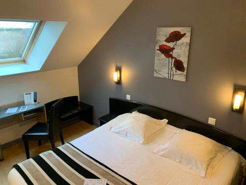 a bedroom with a bed and a desk and a window at Hôtel Le Bayeux in Bayeux