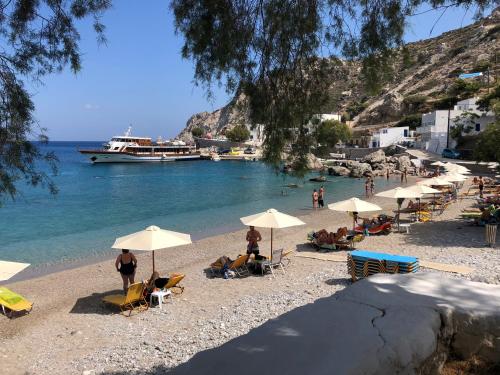 a group of people sitting on a beach with umbrellas at TO VOTSALO-beach side studios & taverna in Karpathos Town