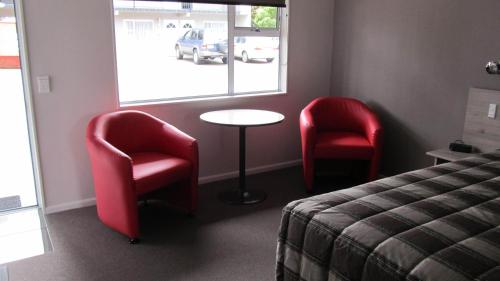 a room with two chairs and a table and a bed at Carramar Motor Inn in Palmerston North