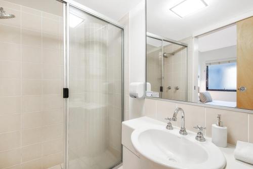 a bathroom with a shower, sink, and mirror at Beach Club Resort Mooloolaba in Mooloolaba